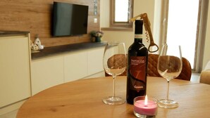 A bottle of Valpolicella wine, two wine glasses, and a lit candle on a wooden table in a room with a TV on the wall. - SUPERIOR SUITE, Verona | 1K_HOME (Bosco Chiesanuova)