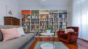 Una sala de estar con un sofá gris, un sillón rojo, una estantería llena de libros y una mesita con una planta.