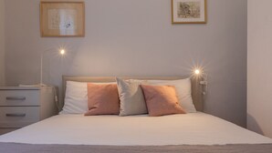 Una cama bien hecha con dos almohadas, una lámpara de noche y dos cuadros en la pared.
