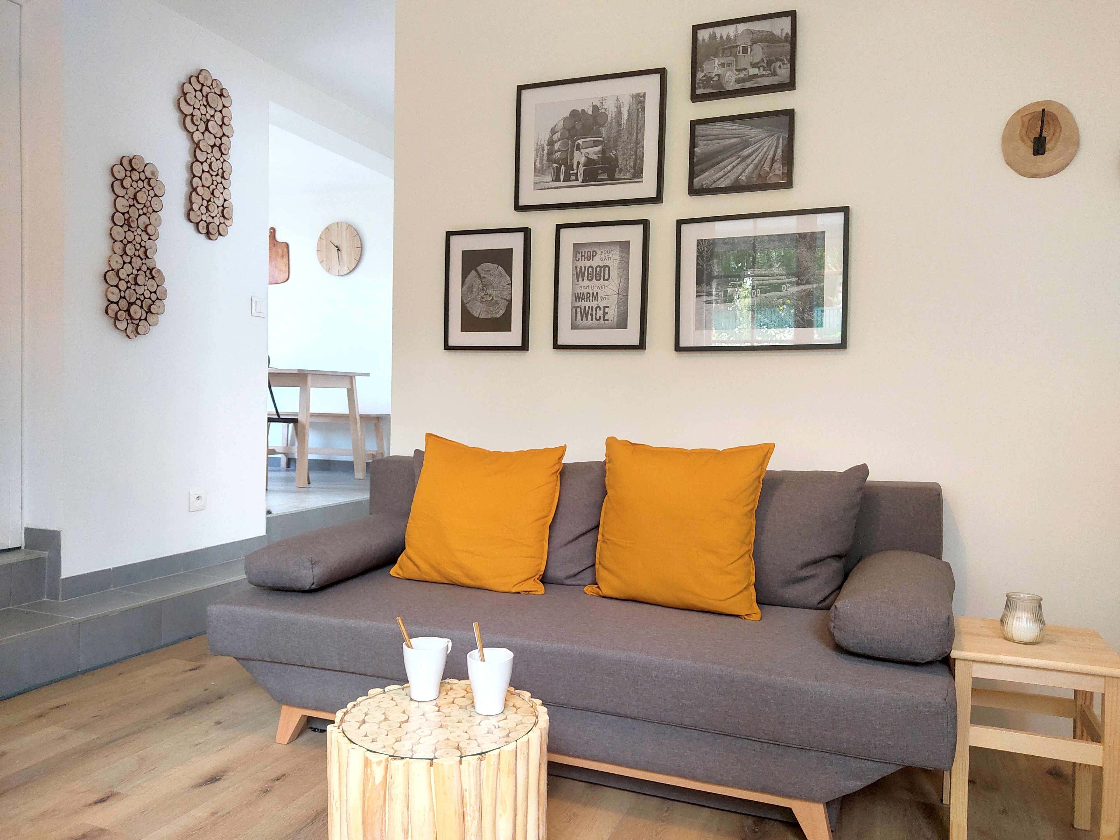 A modern living room with a grey sofa, two mustard pillows, and a round wooden coffee table with two white cups.