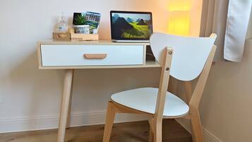 Een houten bureau met een laptop, een klein plantje en een fles handdesinfectiemiddel.
