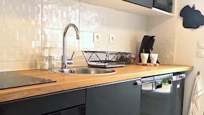 Une cuisine moderne avec un lave-vaisselle noir, un plan de travail en bois et un évier en acier inoxydable.