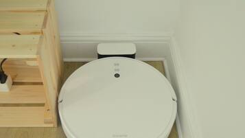 Un dispositivo blanco y circular, compacto, sobre un suelo de madera, probablemente un inodoro inteligente, con un panel de control y un cable de alimentación.