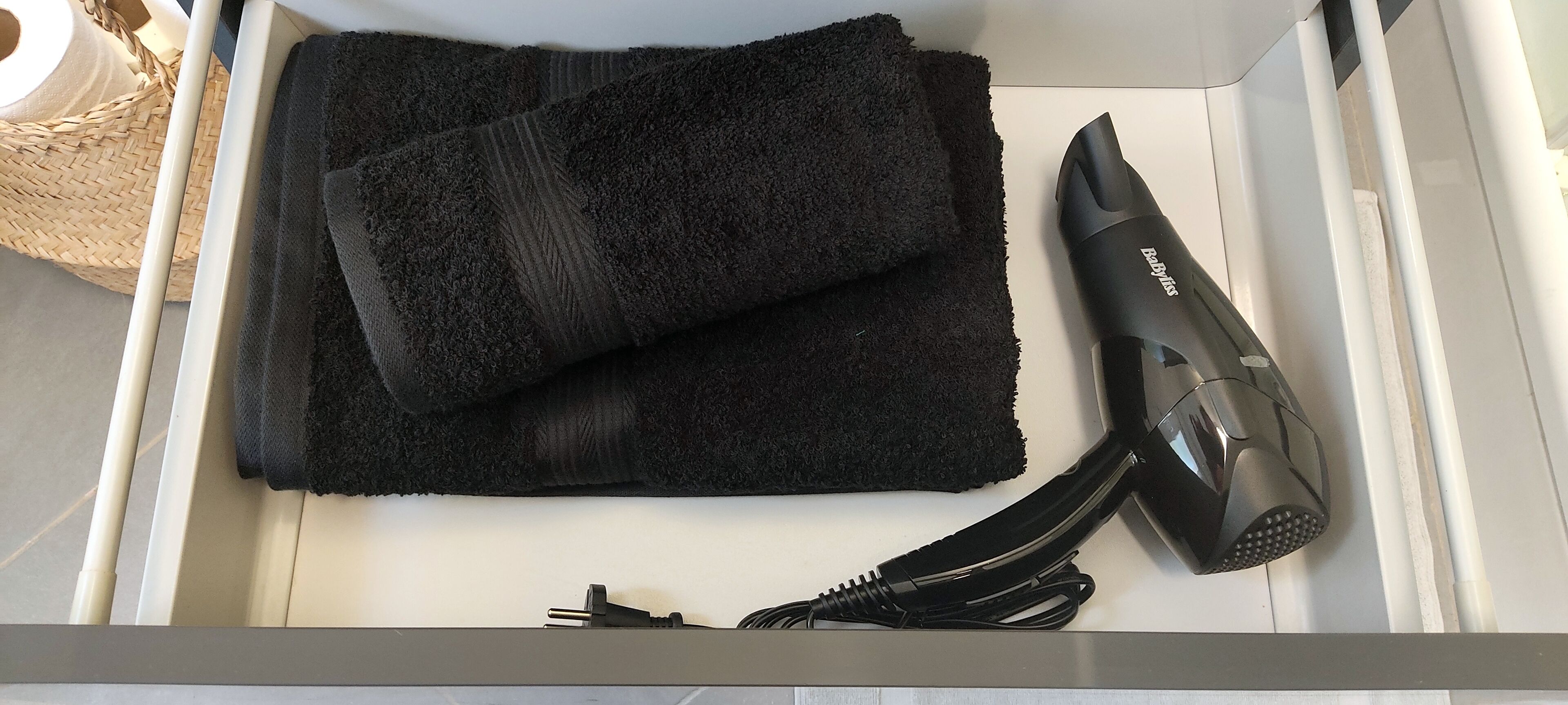 Ein Badezimmer mit einem weißen Waschbecken, einem schwarzen Handtuch und einem Föhn.