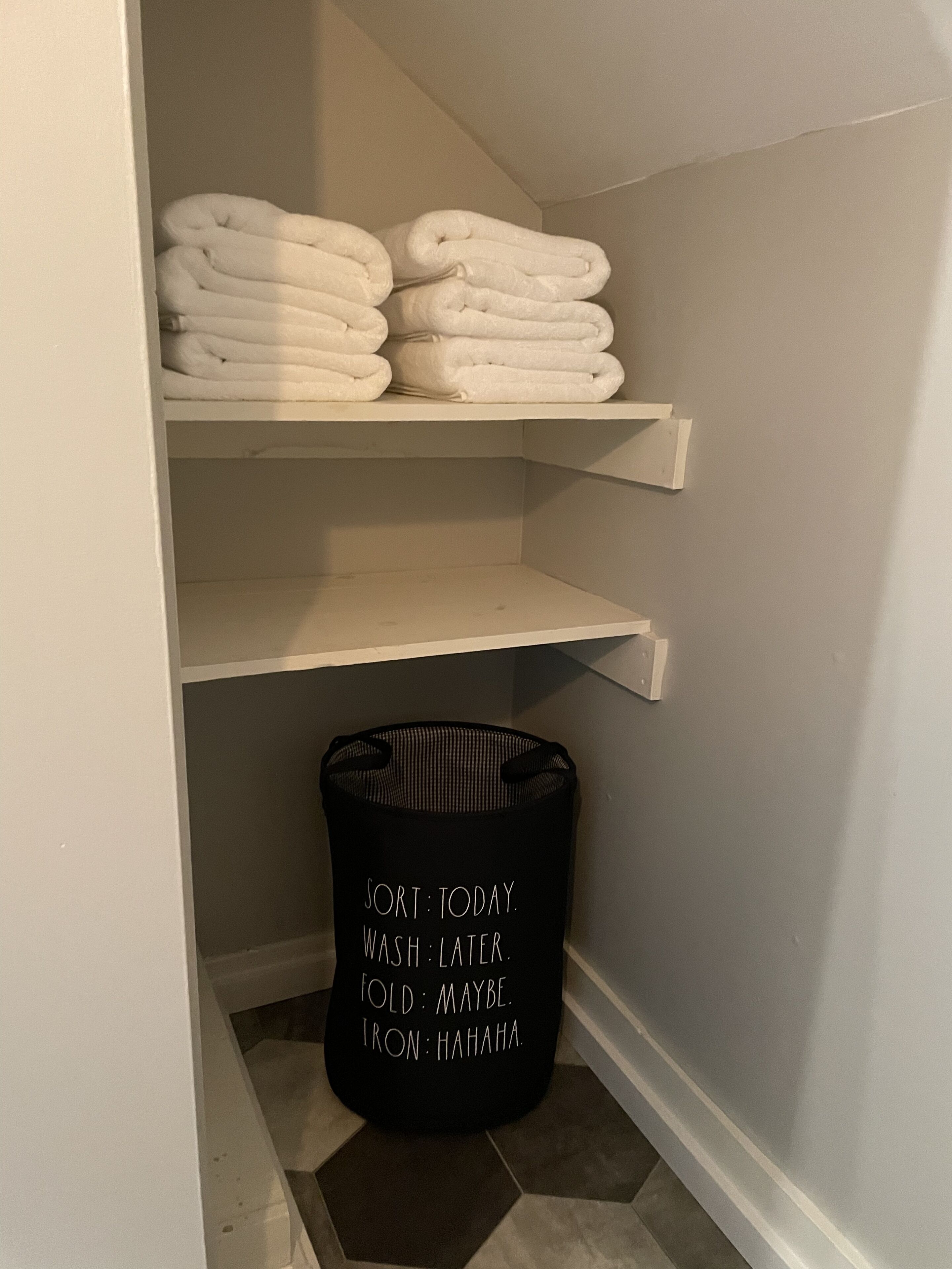 A laundry basket with humorous text and a neatly organized shelf with folded towels.
