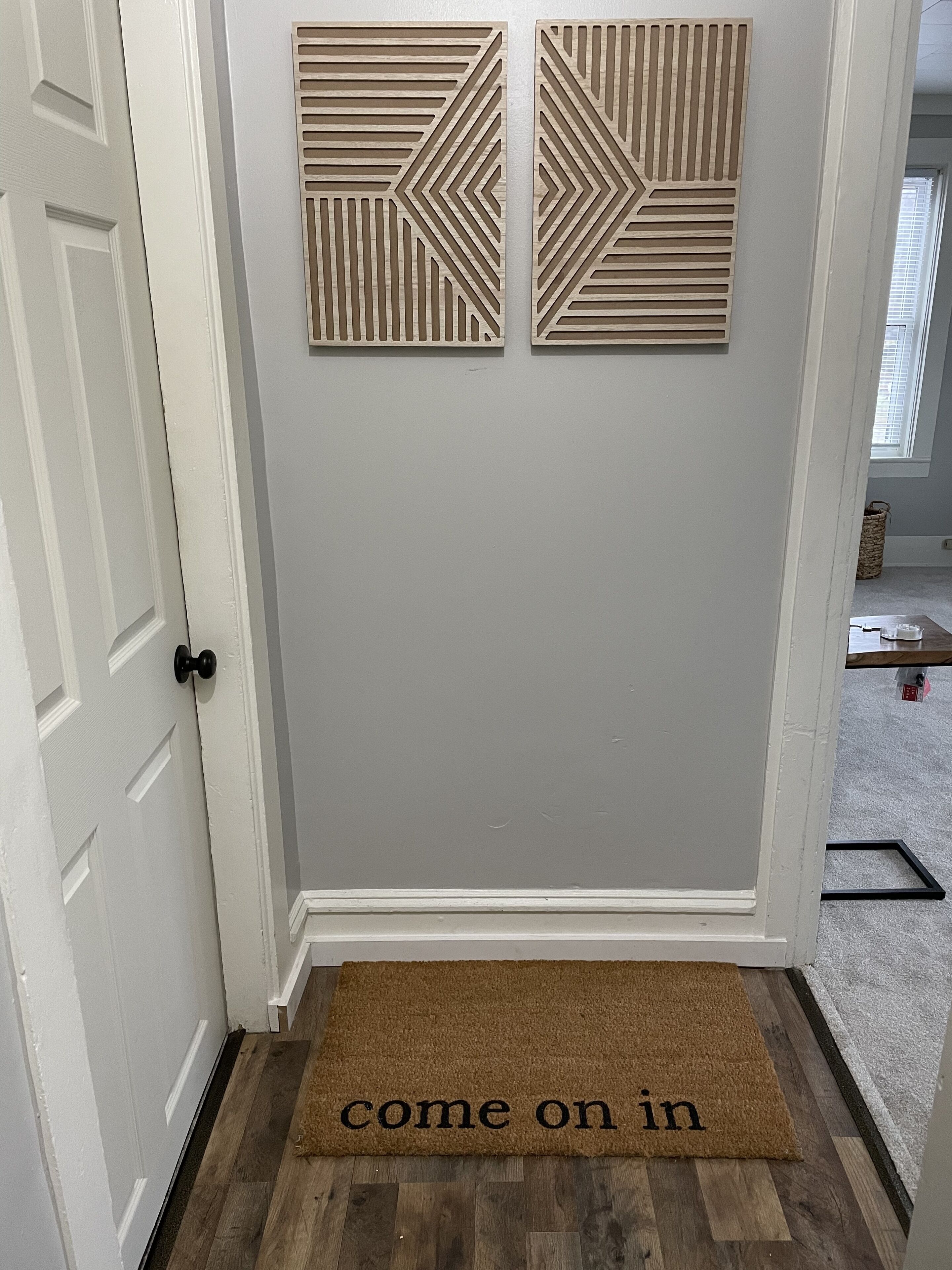 Una porta con decorazione geometrica sopra e un tappetino d'ingresso con la scritta “come on in”.