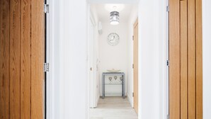 A hallway with wooden doors, a white wall, a clock, and a small table with a vase. - Comfortable 2BR Apartment in Bedford (Bedford)