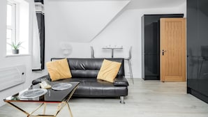 A modern living room with a black leather sofa, a glass coffee table, and a dining area with a small table and chairs. - Comfortable 2BR Apartment in Bedford (Bedford)