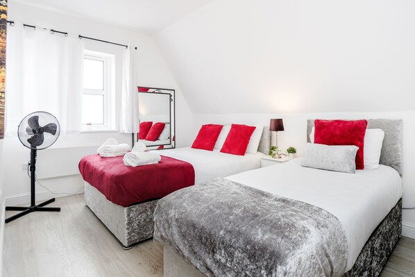A hotel room with two beds, a large mirror, a standing fan, and a window with curtains.