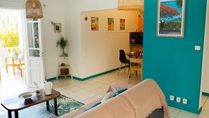 Una sala de estar acogedora con un sofá, una mesita de centro y un comedor con sillas y una mesa. Hay obras de arte en las paredes y una puerta que conduce a otra habitación.