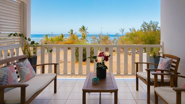 Un balcón con vista a la playa, muebles de madera y plantas en macetas.