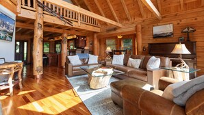 A spacious log cabin interior with a wooden staircase, a living area with sofas and a glass coffee table, and a kitchen area. - Authentic Log Cabin in the Mountains (Seven Devils)