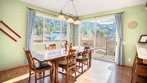 A dining room with a wooden table and chairs, large windows with curtains, and a view of mountains. - Hudson Hideaway, your home away from home (June Lake)