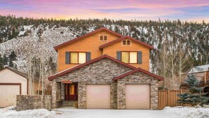 A two-story house with a stone facade, a garage, and a snowy landscape in the background. - Hudson Hideaway, your home away from home (June Lake)