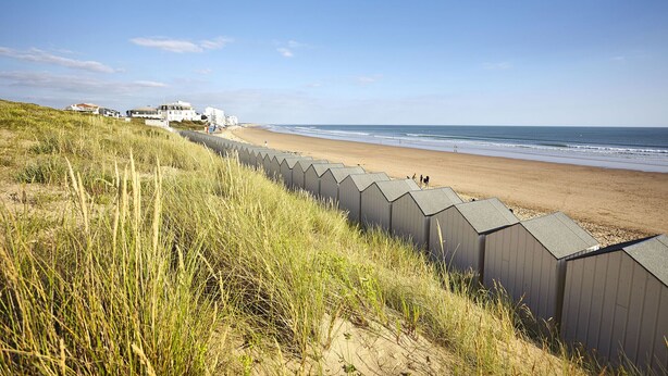 A beach with a dune system and a row of beach huts.