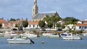 A marina with boats docked, a church with a bell tower, and buildings with red-tiled roofs.