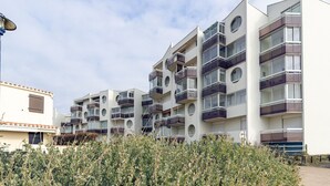 A modern multi-story residential building with balconies, a flat roof, and a clear sky.