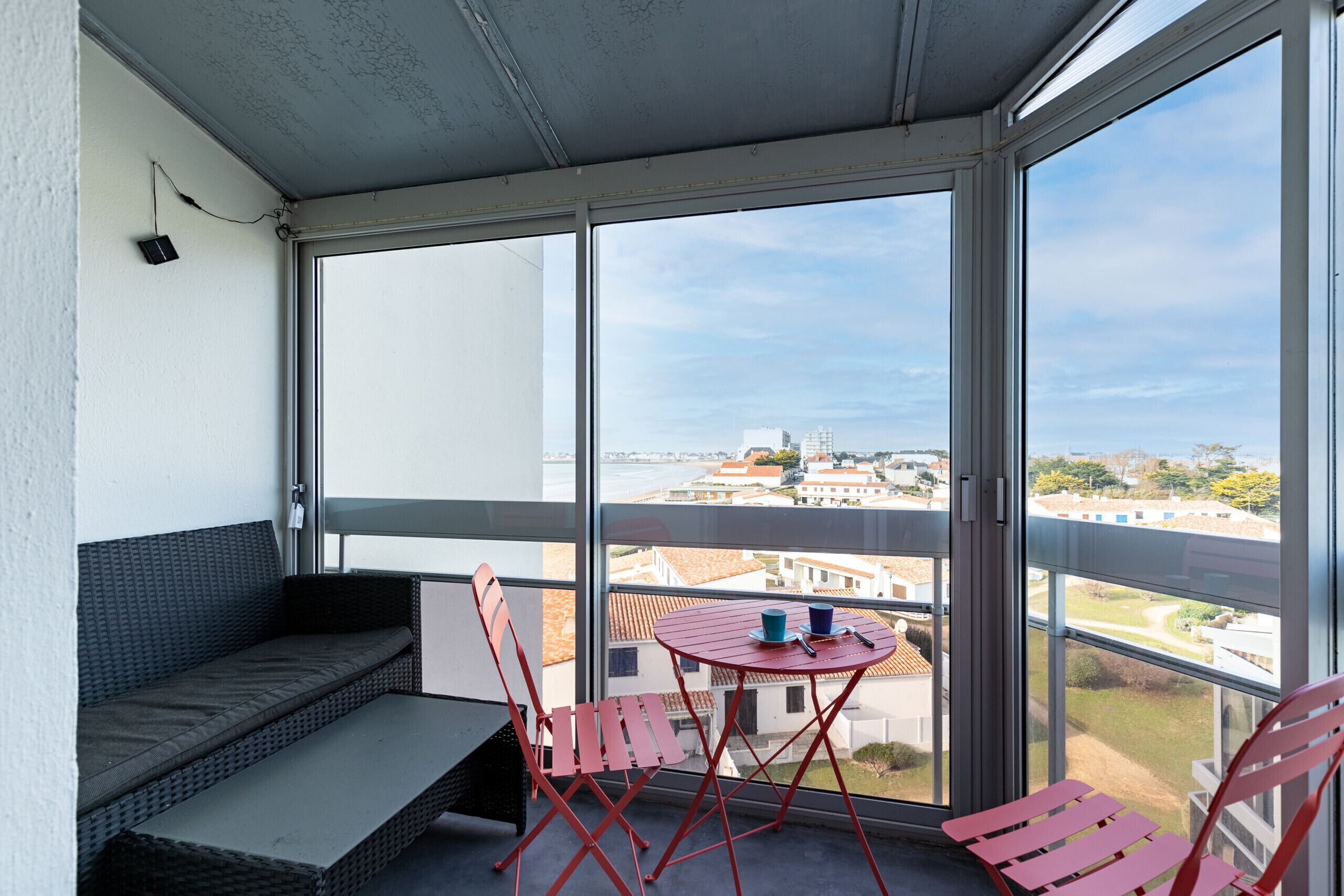 Ein Balkon mit einer Couch, zwei roten Stühlen und einem Tisch mit Tassen.