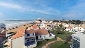 A coastal residential area with white buildings, red-tiled roofs, and a beach in the background.