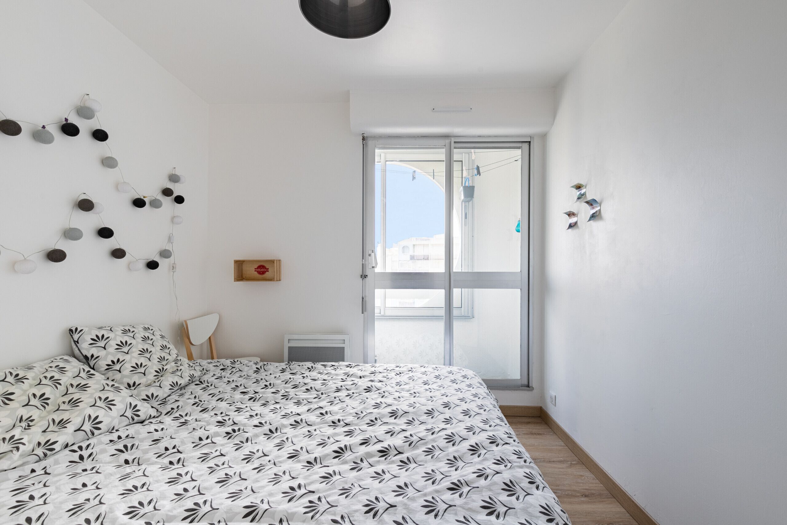 Una camera da letto con un letto, una parete bianca, una finestra e una porta.