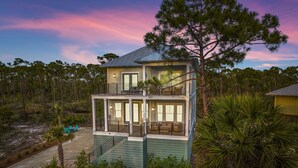 A two-story house with a balcony, surrounded by trees and a natural landscape. - Paradise | Oceanview, Hottub, Shuffleboard, Bikes, Beach, Pool (Port St. Joe)