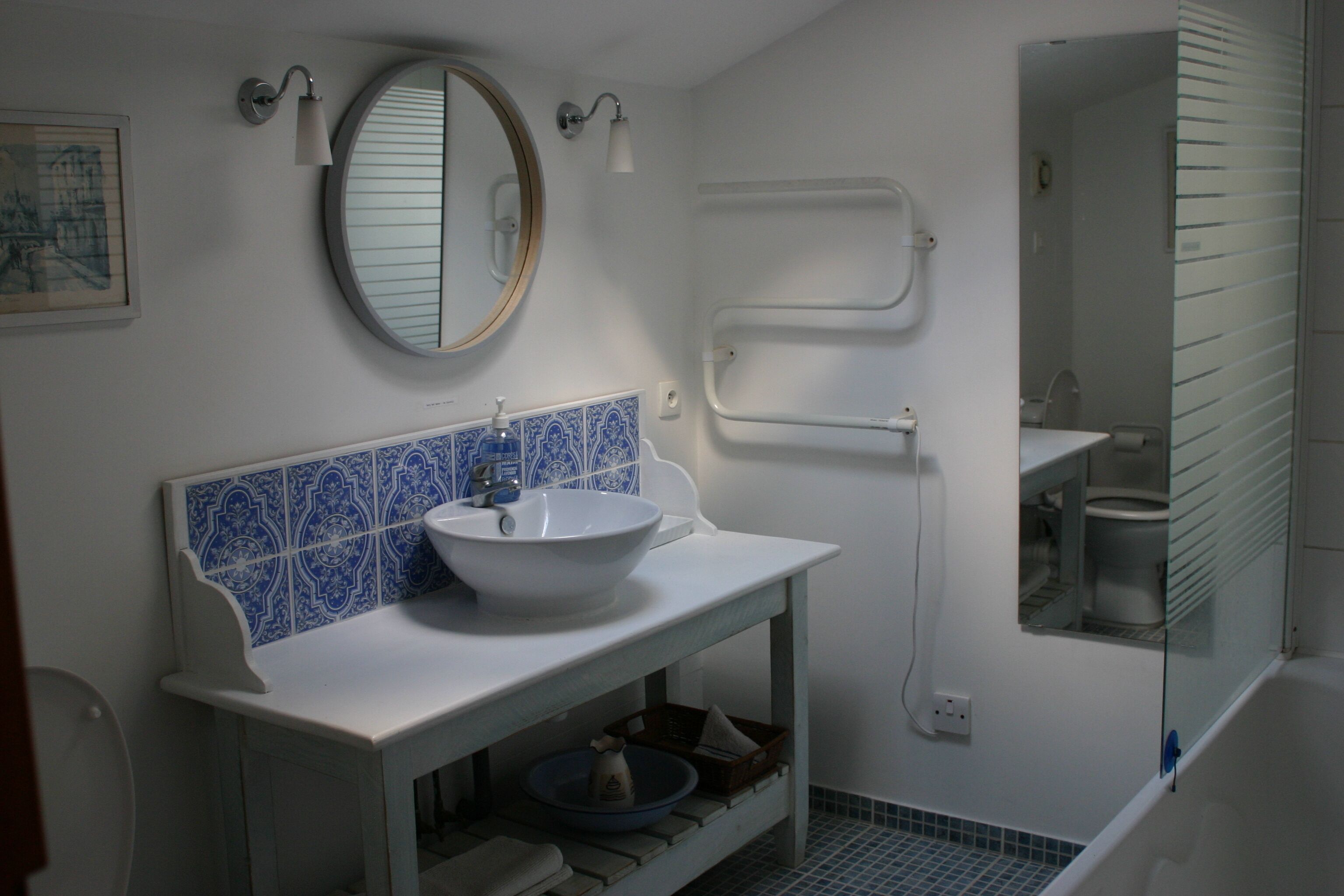 Un bagno con lavandino bianco, piastrelle blu, uno specchio rotondo e una cabina doccia in vetro.