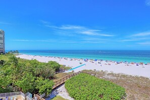 A beach with white sand, clear blue water, and a wooden walkway leading to the shore. - Beachfront Condo | Restaurant, Pool, Spa & Gym (Marco Island)