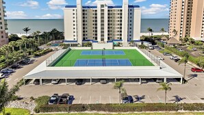 A hotel with a tennis court, parking, and a view of the ocean. - Beachfront Condo | Restaurant, Pool, Spa & Gym (Marco Island)