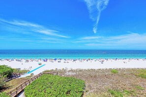 A beach with white sand, clear blue water, and a wooden boardwalk leading to the shore.