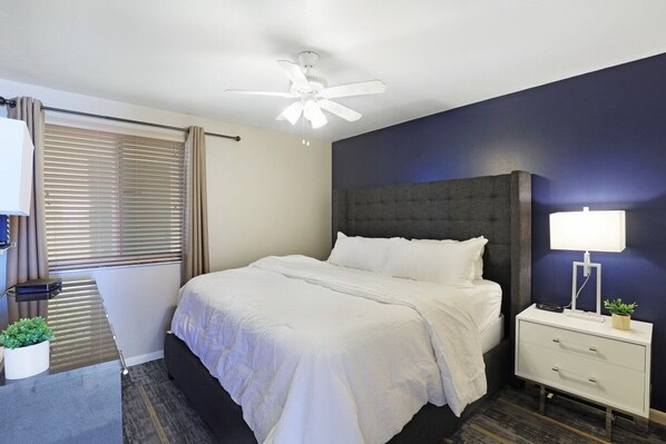 A neatly arranged bedroom with a bed, bedside table, and a ceiling fan.