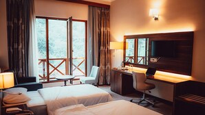 A hotel room with two beds, a desk with a computer, a chair, a TV, and a balcony with a view of trees. - Grand Selale Hotel (Çayeli)