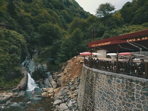 Cafetería de paredes de piedra con terraza exterior y vistas a una cascada.