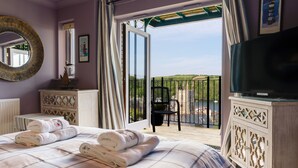 A hotel room with a bed, a TV, a balcony with a view of the countryside, and a window with curtains. - Stunning house, river views, 3 balconies, Fowey (Fowey)
