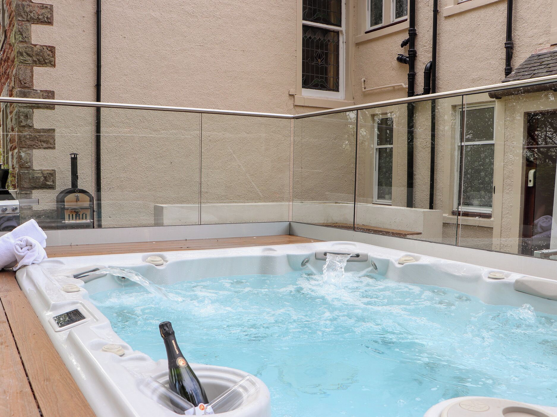 Un jacuzzi con una botella de champán, rodeado de muros de piedra y una terraza de madera.