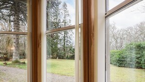 Une vue à travers une fenêtre avec un cadre en bois, donnant sur un espace verdoyant avec des arbres et un banc.