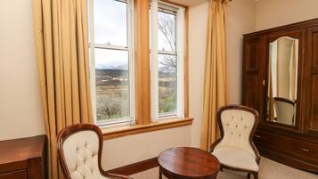 A room with two upholstered chairs, a wooden table, a large mirror, and a window with curtains.
