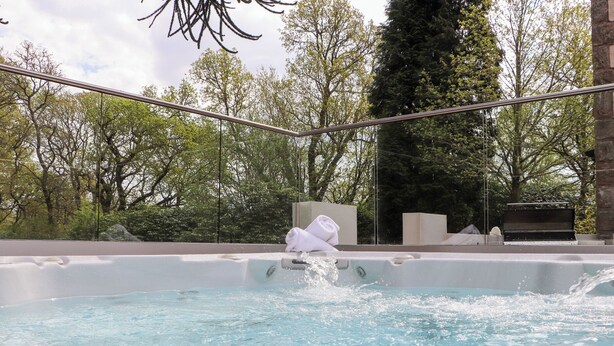 Un bain à remous avec vue sur les arbres et une structure en pierre en arrière-plan.