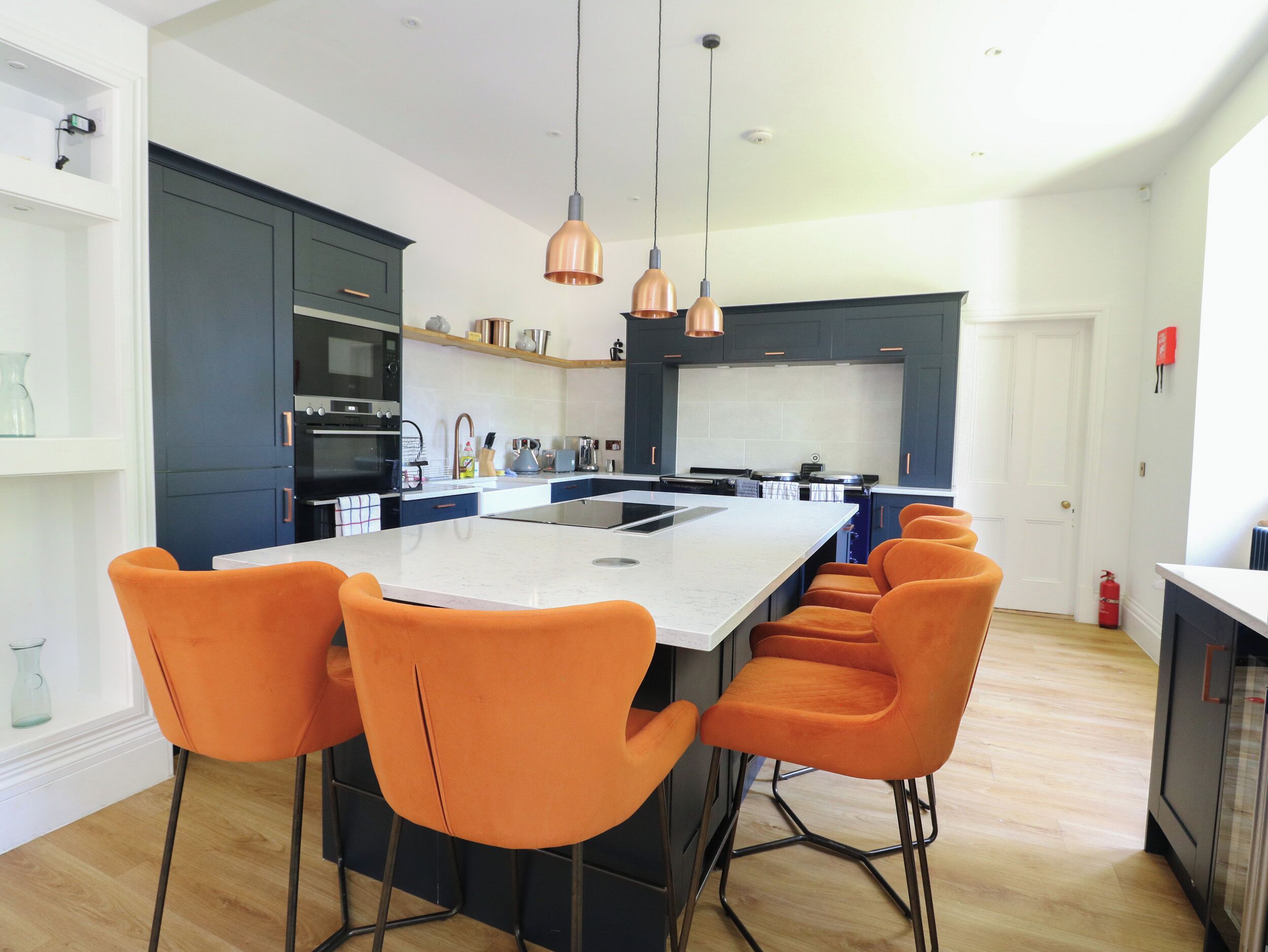 Une cuisine moderne avec un îlot central, des meubles de couleur sombre et des chaises orange.