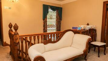Una habitación con escalera de madera, un banco acolchado, una mesa con objetos y una ventana con cortinas.