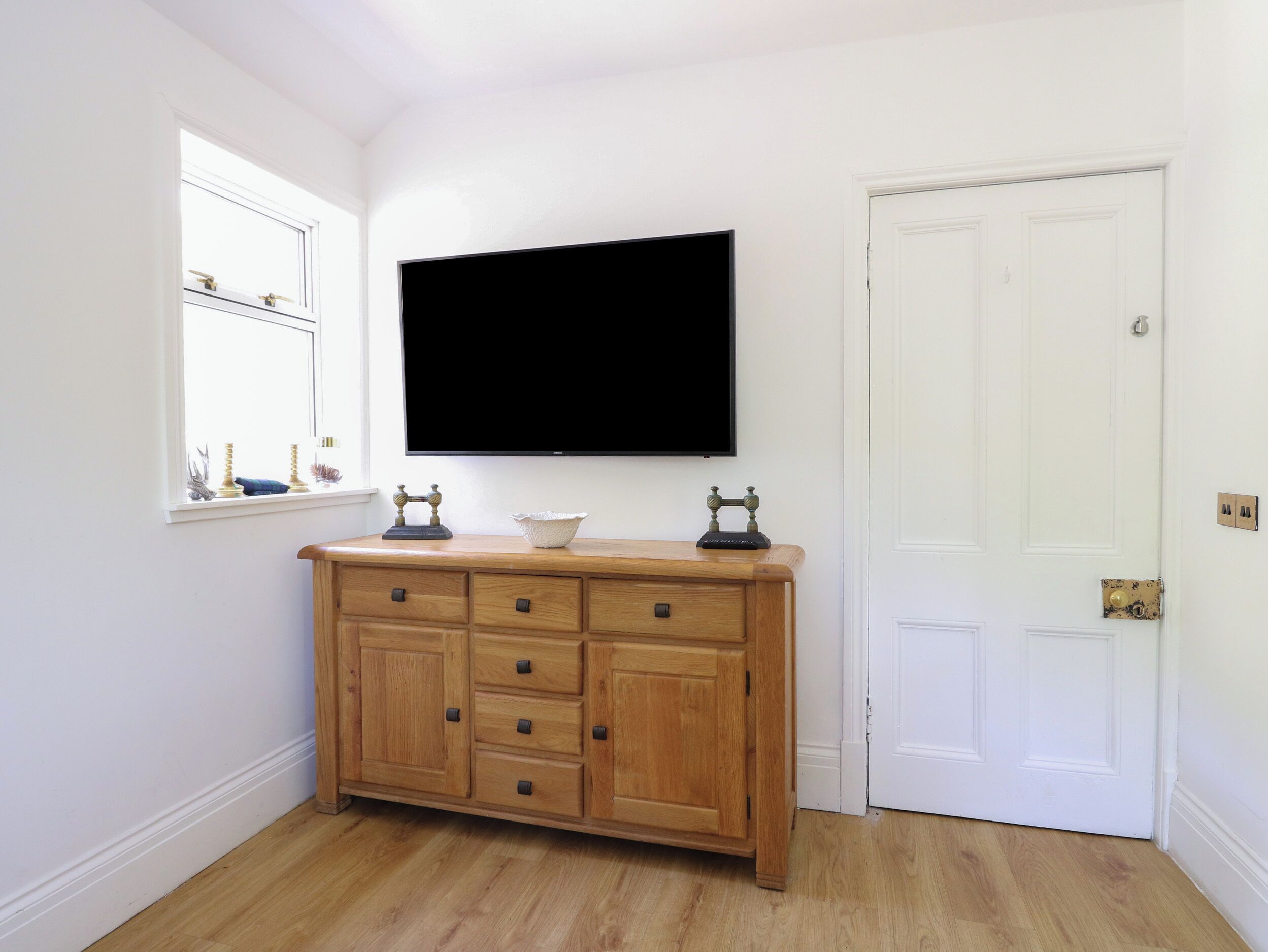 Una habitación con un armario de madera, un televisor montado en la pared, una puerta y una ventana con adornos.