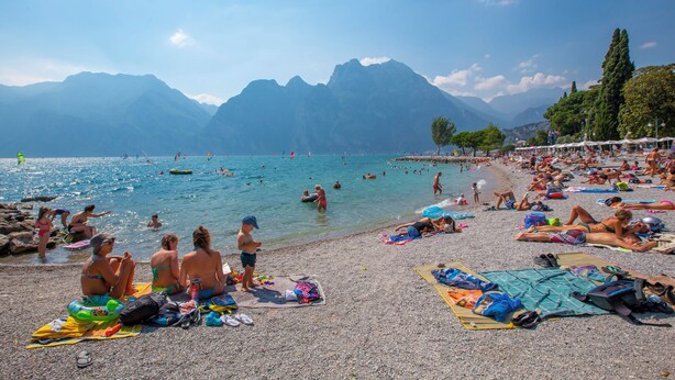 A crowded beach with people sunbathing and swimming, surrounded by mountains. - Les Suites Di Sara Rooms (Riva del Garda)