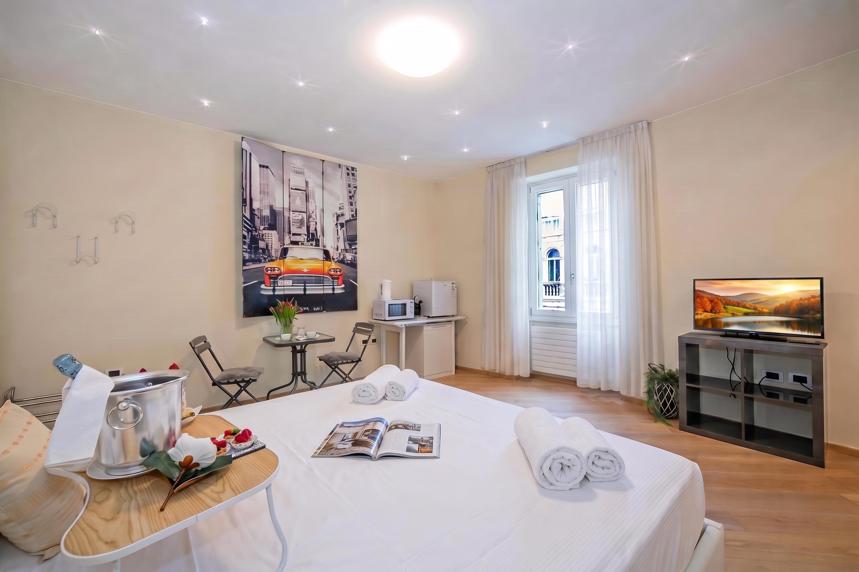 Een hotelkamer met een bed, een eettafel met een tijdschrift, een televisie en een raam met gordijnen.