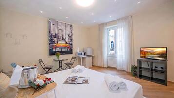Een hotelkamer met een bed, een eettafel met een tijdschrift, een televisie en een raam met gordijnen.