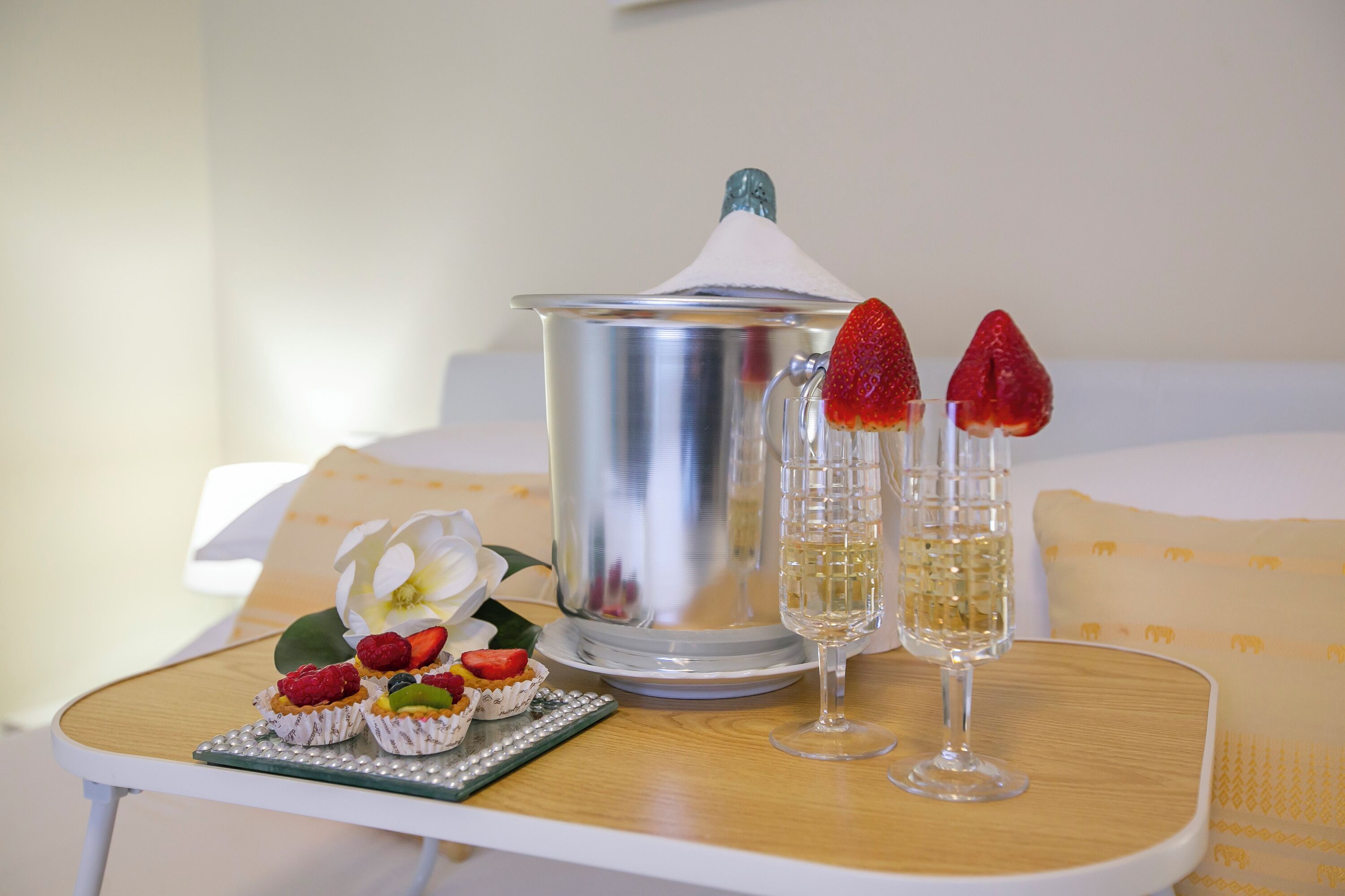 Een dienblad met een zilveren pot, twee champagneglazen en een bord met fruitgebakjes.
