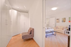 Une chambre à coucher moderne avec un lit, un canapé et un fauteuil. On y trouve des armoires blanches et un miroir.