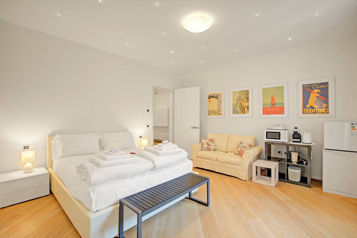 Een moderne hotelkamer met een opgemaakt bed, een kleine zithoek, een eethoek met een magnetron en koffiezetapparaat, en kunstwerken aan de wanden.