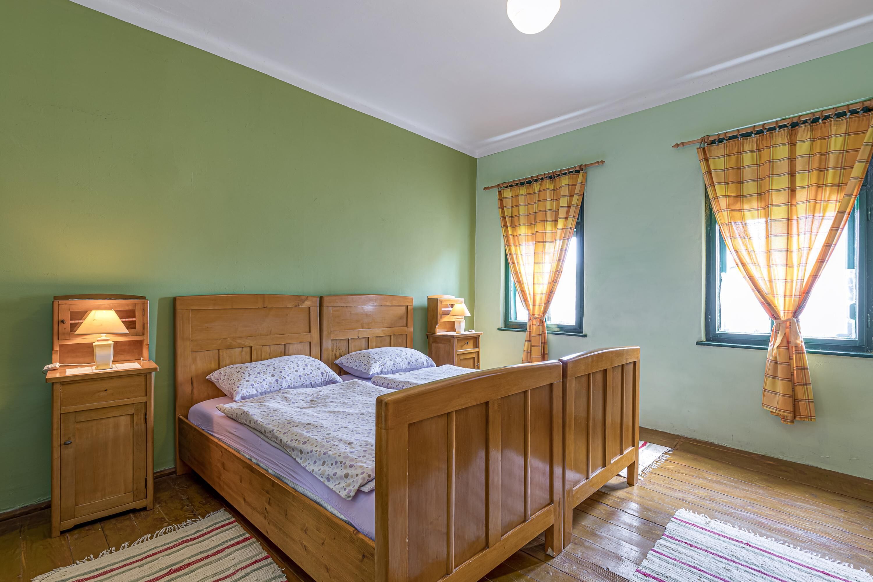 Une chambre avec un lit en bois, deux tables de chevet avec des lampes, une fenêtre avec des rideaux et un plancher en bois.