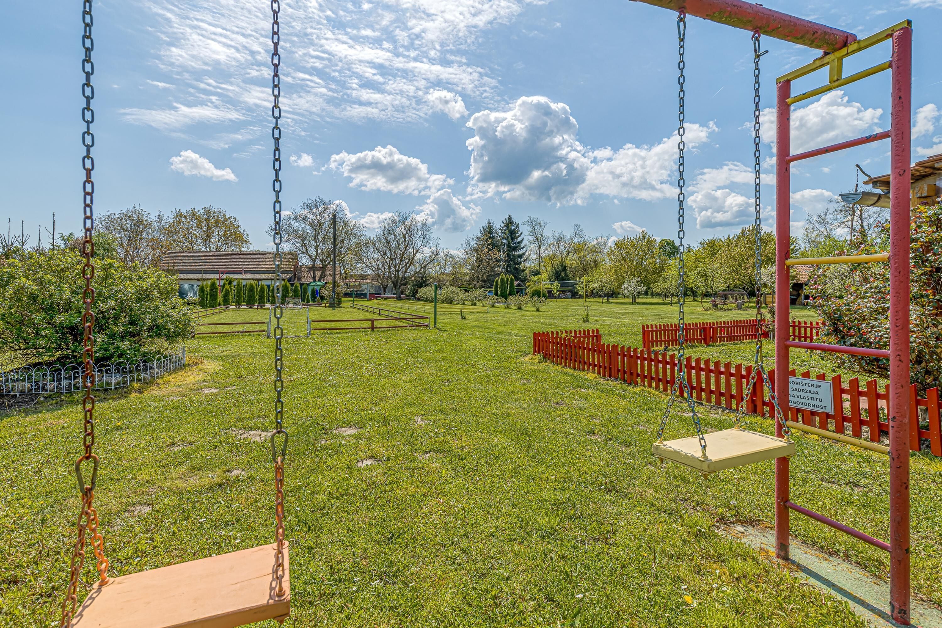 A playground with swings and a red fence.