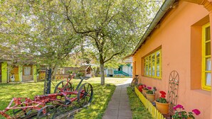 A pathway leading to a building with a yellow window trim, a bicycle, and potted plants. - Traditional Child Friendly Homestead Larva (Velika)