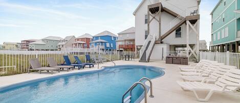 A swimming pool with lounge chairs, a staircase, and a white building with a blue roof.